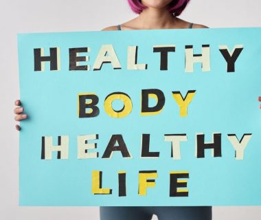 A woman holds a motivational poster advocating a healthy body and life for wellness.